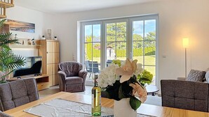 Una sala de estar moderna con comedor, ventanas grandes y vistas a un jardín.