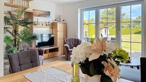 Una sala de estar amplia con una escalera de madera, televisor, sofá y una mesa de comedor con un jarrón de flores.