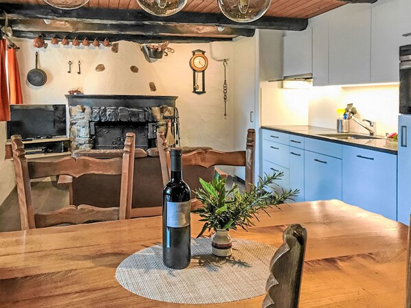 Une cuisine rustique avec une cheminée en pierre, des meubles en bois et une table à manger agrémentée d’une bouteille et d’une plante.