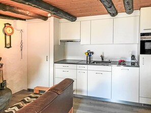 Une cuisine moderne avec des armoires blanches, un comptoir noir et un four encastré. Le plafond est en bois et il y a une horloge au mur.