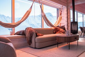 A cozy room with a sofa, a round wooden table, and a large window with a view of snow-capped mountains.