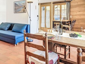Ein Essbereich mit einem Holztisch, gedeckt für zwei Personen, einem blauen Sofa und einem Gemälde einer Berglandschaft an der Wand.