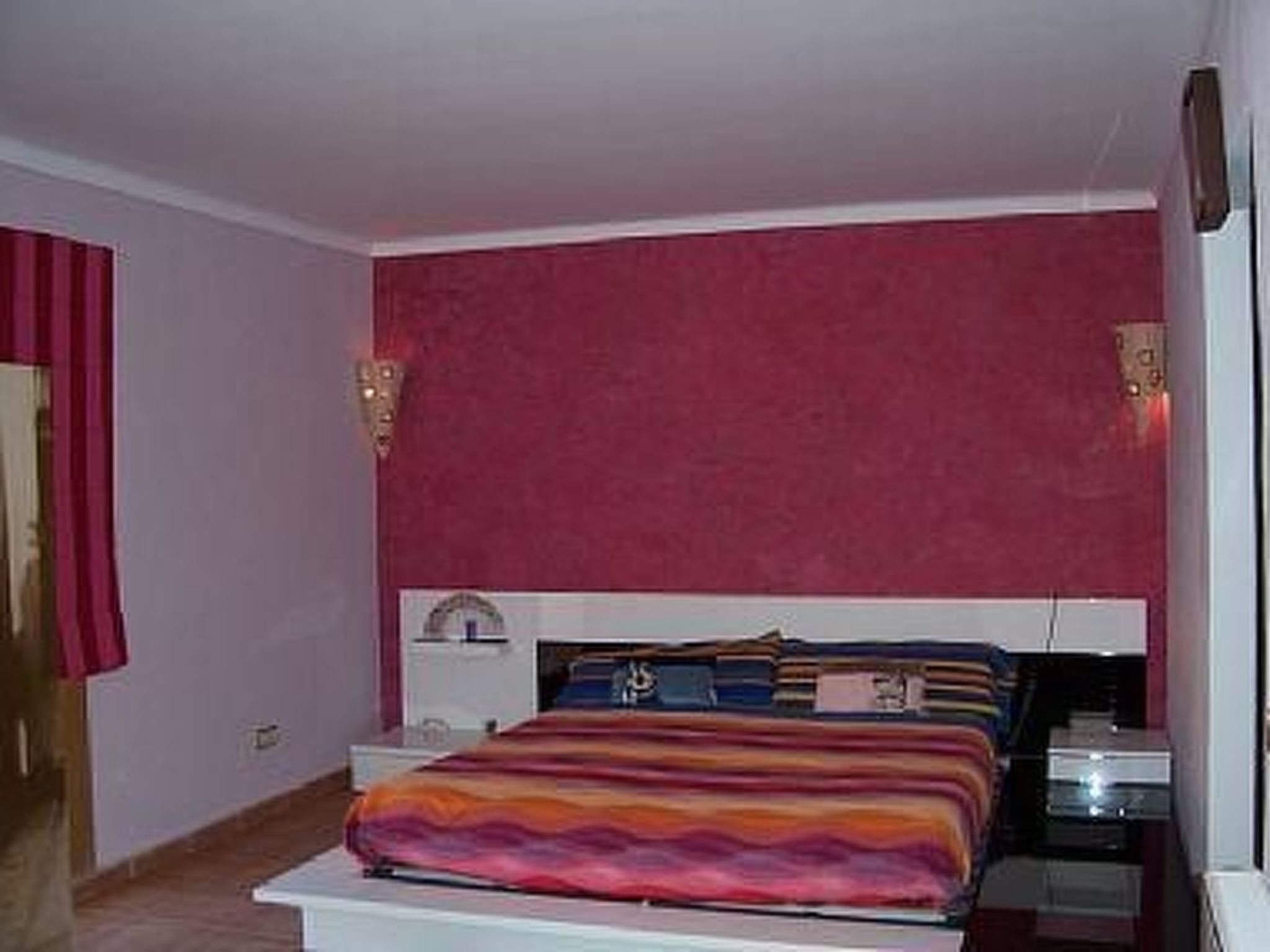 A bedroom with a bed, a nightstand, and a wall-mounted lamp.