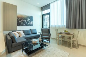 A modern living room with a sofa, coffee table, and dining table with chairs. - Skyline Luxury 1BR - Balcony (Dubai)