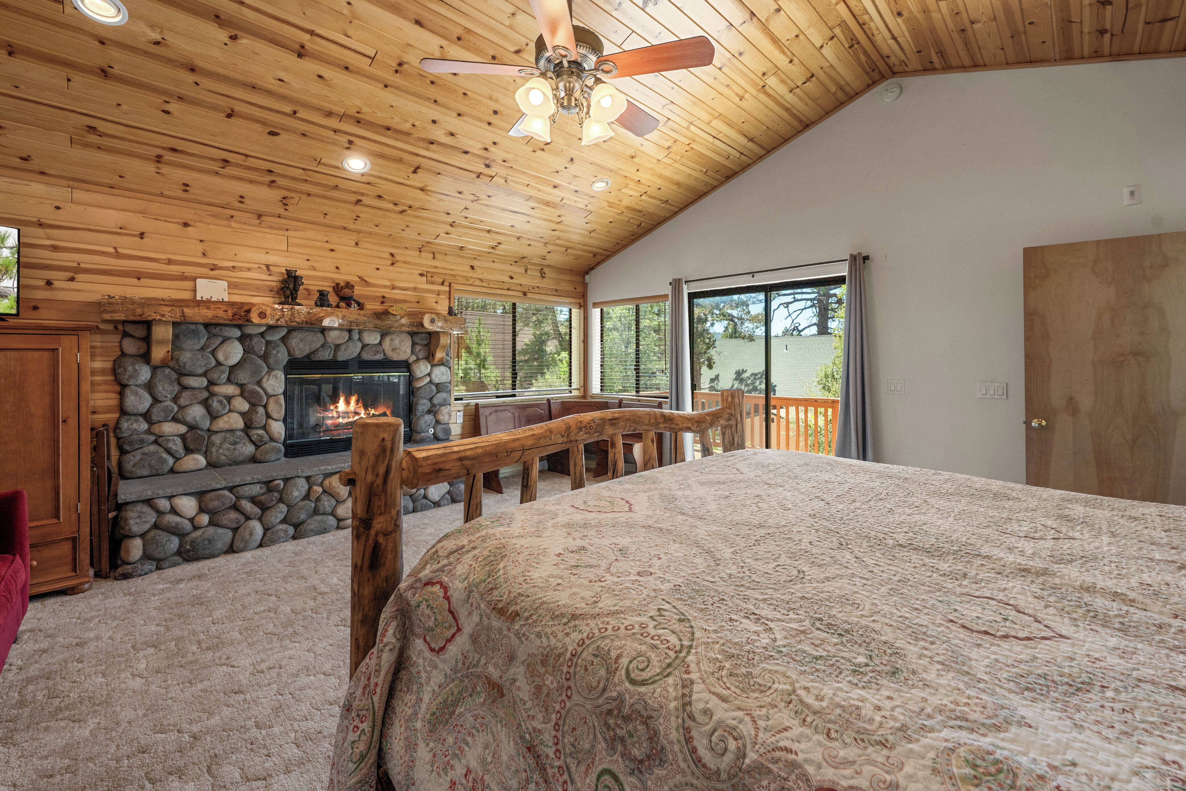 Interno di una baita in legno con camino in pietra, soffitto in legno e un letto grande.