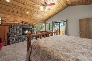 A log cabin interior with a stone fireplace, wooden ceiling, and a large bed. - Spacious Log Cabin w/ Game Room & AC Near Bear Mountain (Big Bear City)