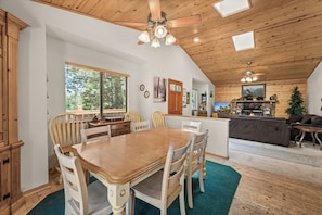 A spacious dining area with a wooden table and chairs, a kitchen in the background, and a ceiling fan. - Spacious Log Cabin w/ Game Room & AC Near Bear Mountain (Big Bear City)