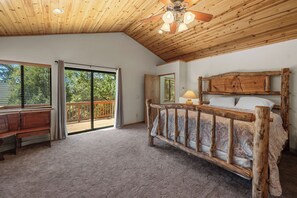 A bedroom with a wooden ceiling, a wooden bed frame, a bench, and a view through a sliding glass door to an outdoor deck. - Spacious Log Cabin w/ Game Room & AC Near Bear Mountain (Big Bear City)