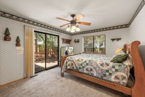A bedroom with a bed, a ceiling fan, a window, and a door leading to an outdoor area. - Spacious Moonridge Log Cabin with A/C, Game Room, 2 Fireplaces & Fenced Yard (Big Bear City)