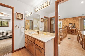 A bathroom with a wooden vanity, a large mirror, and a wooden dining area with chairs. - Lakeview Mountain Retreat w/ Balcony, Gas Fire Pit, Pool table, Walk to Lake (Fawnskin)