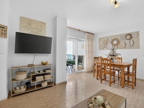 A living room with a flat-screen TV, wooden dining table, chairs, and a coffee table. - Los Ibicencos by Interhome (La Manga del Mar Menor)