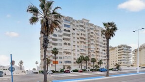 Un immeuble résidentiel à plusieurs étages, doté de balcons, de palmiers et d’une piste cyclable bleue.