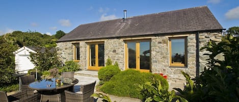 Une maison en pierre avec un patio carrelé, une table à manger et des chaises en osier.