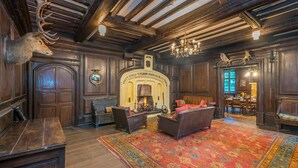 Una sala amplia con chimenea, paneles de madera, un candelabro y un gran tapete.