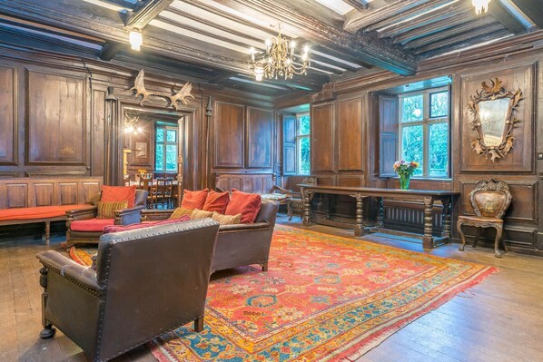 A spacious room with wooden paneling, a large ornate chandelier, and a patterned rug.