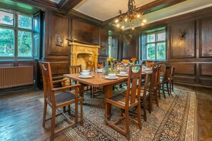 A dining room with a wooden table set for six, surrounded by chairs, a fireplace, and a chandelier.