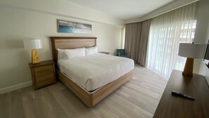 Hotellihuone, jossa on puinen sänky, yöpöytä lampun kanssa, työpöytä lampun kanssa ja suuret ikkunat, joista on näkymä ulos.