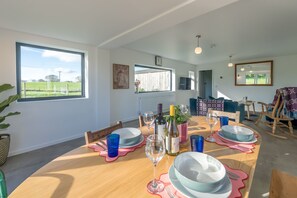Ein Essbereich mit einem Holztisch, gedeckt für vier Personen, umgeben von Stühlen, mit Blick auf ein grünes Feld durch große Fenster.