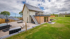 Une maison moderne dotée d’une grande terrasse, d’un jacuzzi extérieur et d’un escalier menant à un deuxième étage.