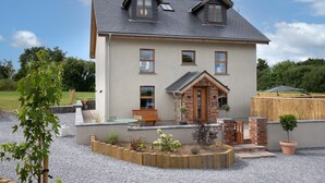 Une maison à deux étages avec un porche à l’avant, une clôture en bois et une allée gravillonnée.