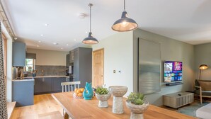 Une cuisine moderne avec des meubles de couleur sombre, une table à manger en bois et des luminaires suspendus.