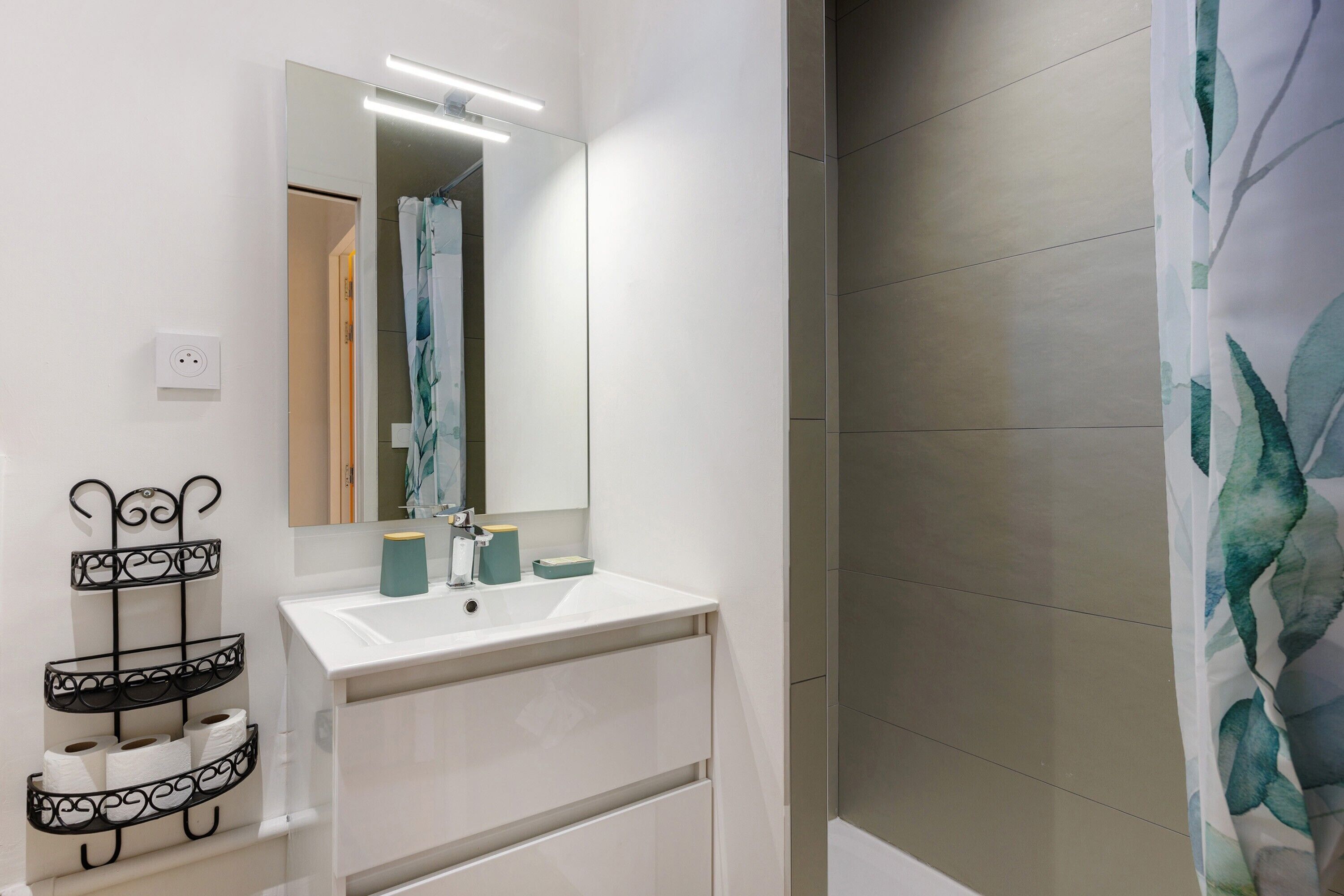 Une salle de bain avec un lavabo blanc, un miroir, un porte-serviettes et un rideau de douche.