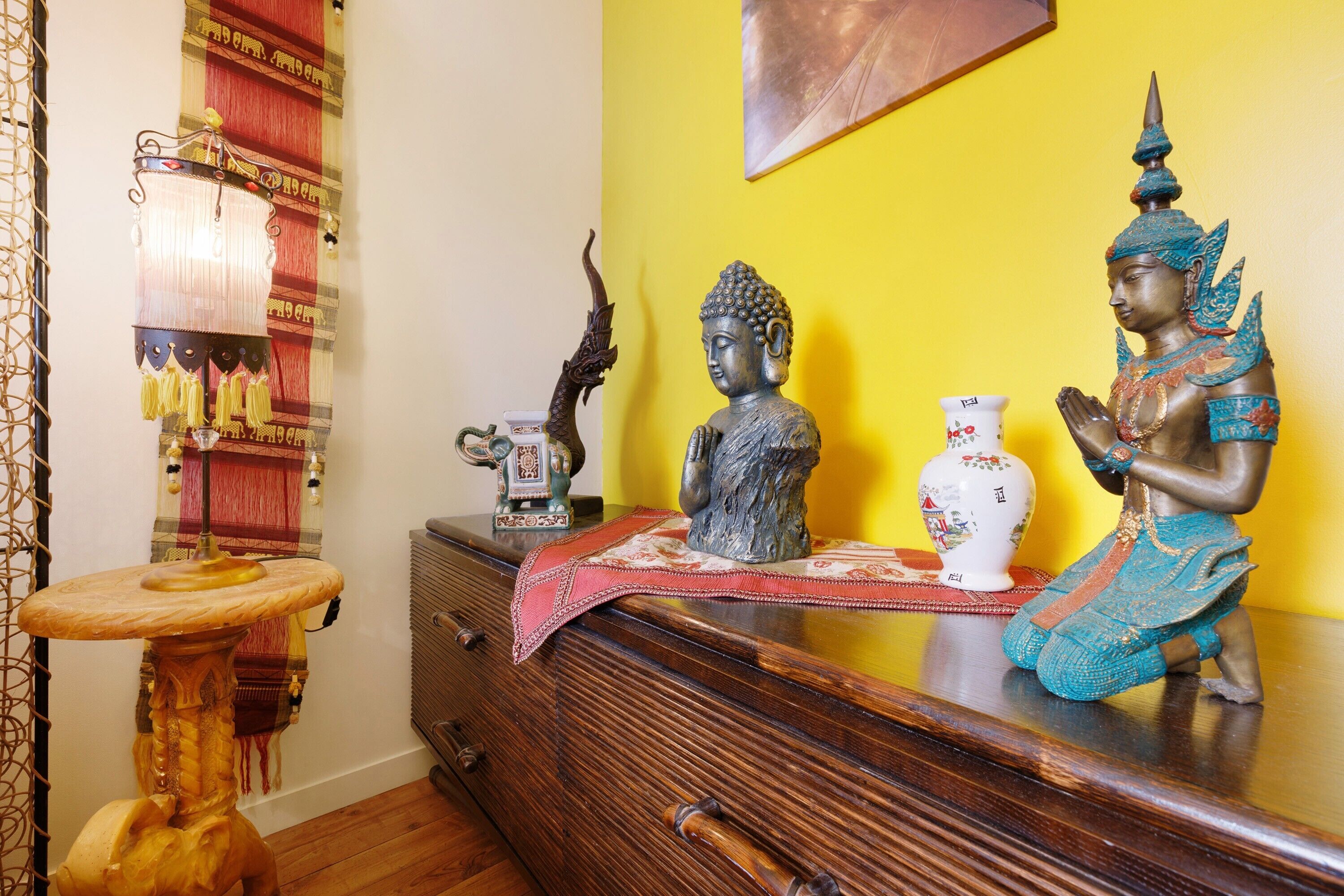 Un aparador de madera con una estatua de Buda, un jarrón decorativo y una mesita con un mantel.