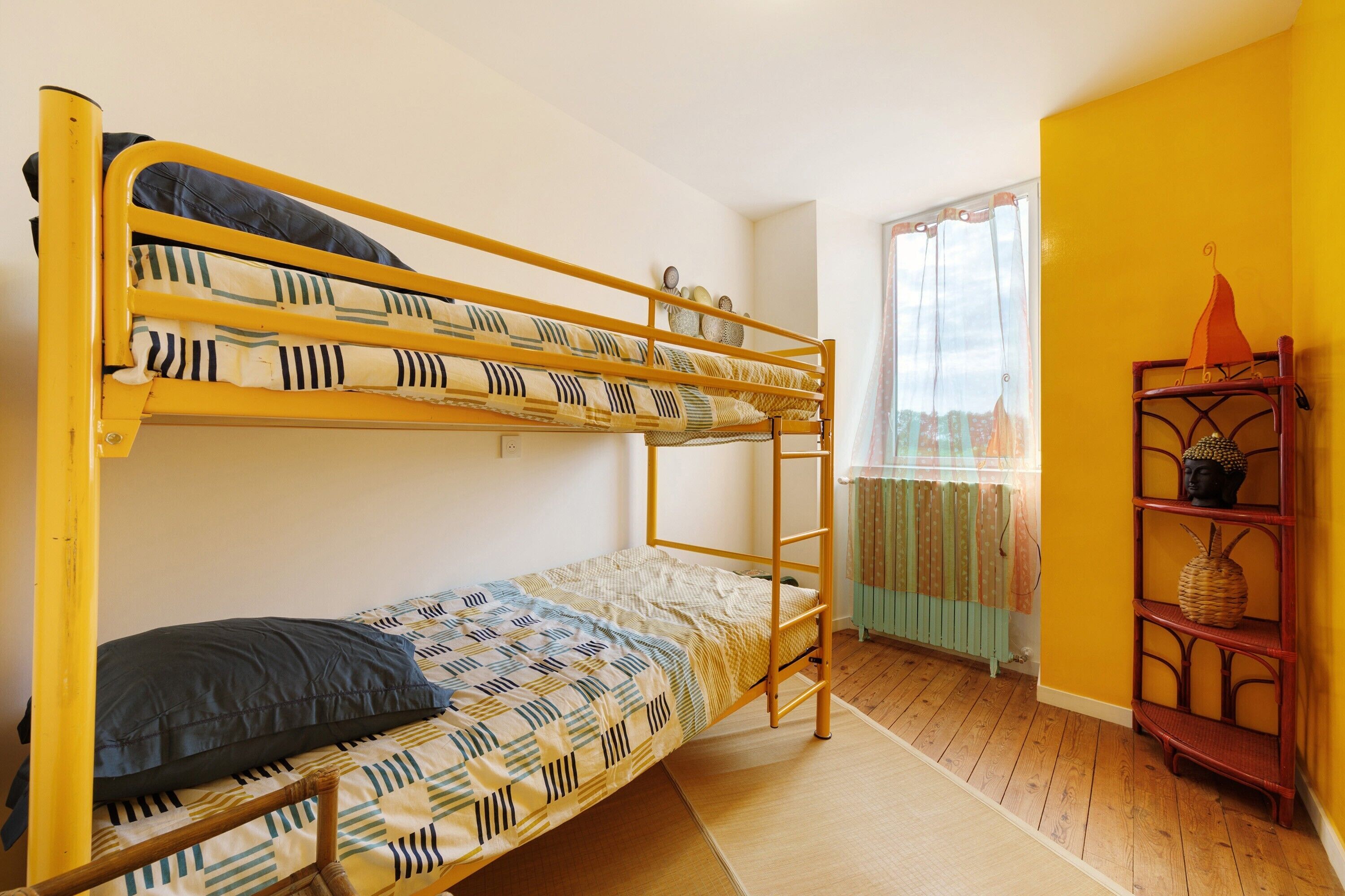 A bunk bed room with a window, a wooden floor, and a shelf with decorative items.