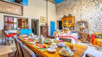 A dining area with a long wooden table set for a meal, stone walls, and a view of the sky.
