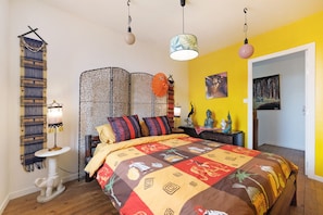 A room with a bed, a small table, a decorative wall hanging, a partition, and a painting. - Guest Room 'Les Philous Gourmands - Thailand' with Private Garden and Wi-Fi (Sèvremont)