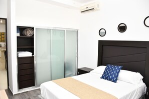 Quarto de hotel com uma cama, um guarda-roupa com portas deslizantes, uma mesa de cabeceira e um ar condicionado fixado na parede.