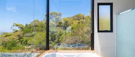 A modern bathroom with a glass-enclosed hot tub and a view of a forested hillside.
