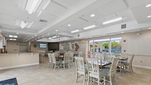 A spacious dining area with multiple tables and chairs, a reception desk, and a view of the outdoors through large windows. - Oceanwalk 1-202 (New Smyrna Beach)