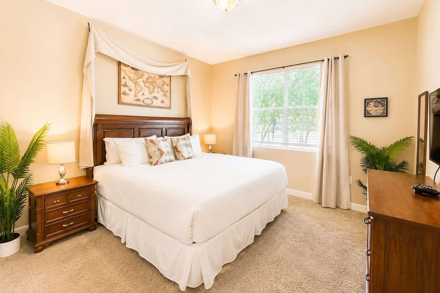 A hotel room with a large bed, a nightstand, a dresser, a TV, and a window with curtains.