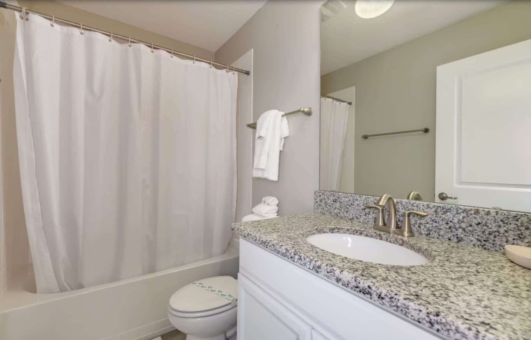 Ein Badezimmer mit Duschvorhang, Toilette, Waschbecken mit Granitplatte und Spiegel.
