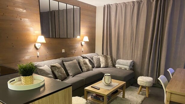 Ein modernes Wohnzimmer mit einem Holzsofa, einem kleinen Couchtisch, einem Beistelltisch, einem flauschigen Hocker und einem Esstisch.