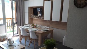 Eine moderne Küche mit Esstisch, gedeckt für vier Personen, weißen Stühlen, einem an der Wand montierten Fernseher und einer Uhr.