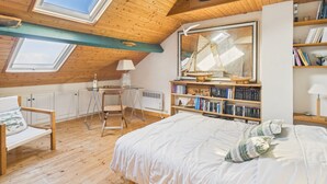 Ett mysigt sovrum på vinden med ett sluttande tak, träbjälkar, ett takfönster, en säng, ett skrivbord och en bokhylla.