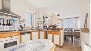 Ett kök med kakelbeklädd vägg bakom arbetsbänken, träskåp, en spis och en matplats med en modell av en segelbåt.
