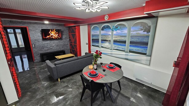 Een moderne woonkamer met een open haard, een bank, een eettafel gedekt voor twee personen en een groot raam met een prachtig uitzicht.