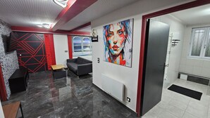 Een modern interieur met een geometrisch wandontwerp, een grijze bank, een schilderij en een deur naar een badkamer.