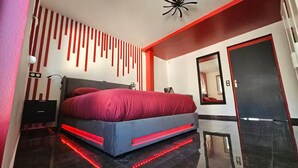 Een moderne slaapkamer met een groot bed, rode verlichting, een spiegel en een zwarte deur.