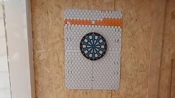 A room with a wooden wall, a dartboard, and a ceiling vent.