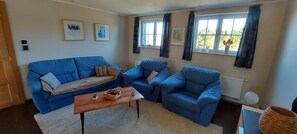 A living room with a blue sofa, a matching armchair, a wooden coffee table, and a window with curtains.