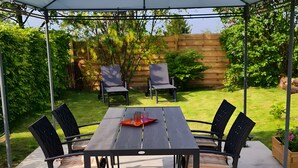 A covered patio with a table and chairs, surrounded by greenery. - Cozy House for 4 in the Heart of the French Ardennes – Laundry, Bike Storage, Near Rocroi & Belgium (Gué-d'Hossus)