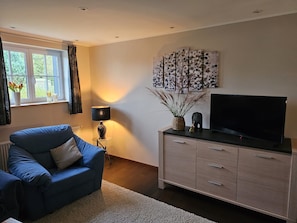 A living room with a sofa, a TV on a cabinet, a lamp, and artwork on the wall.