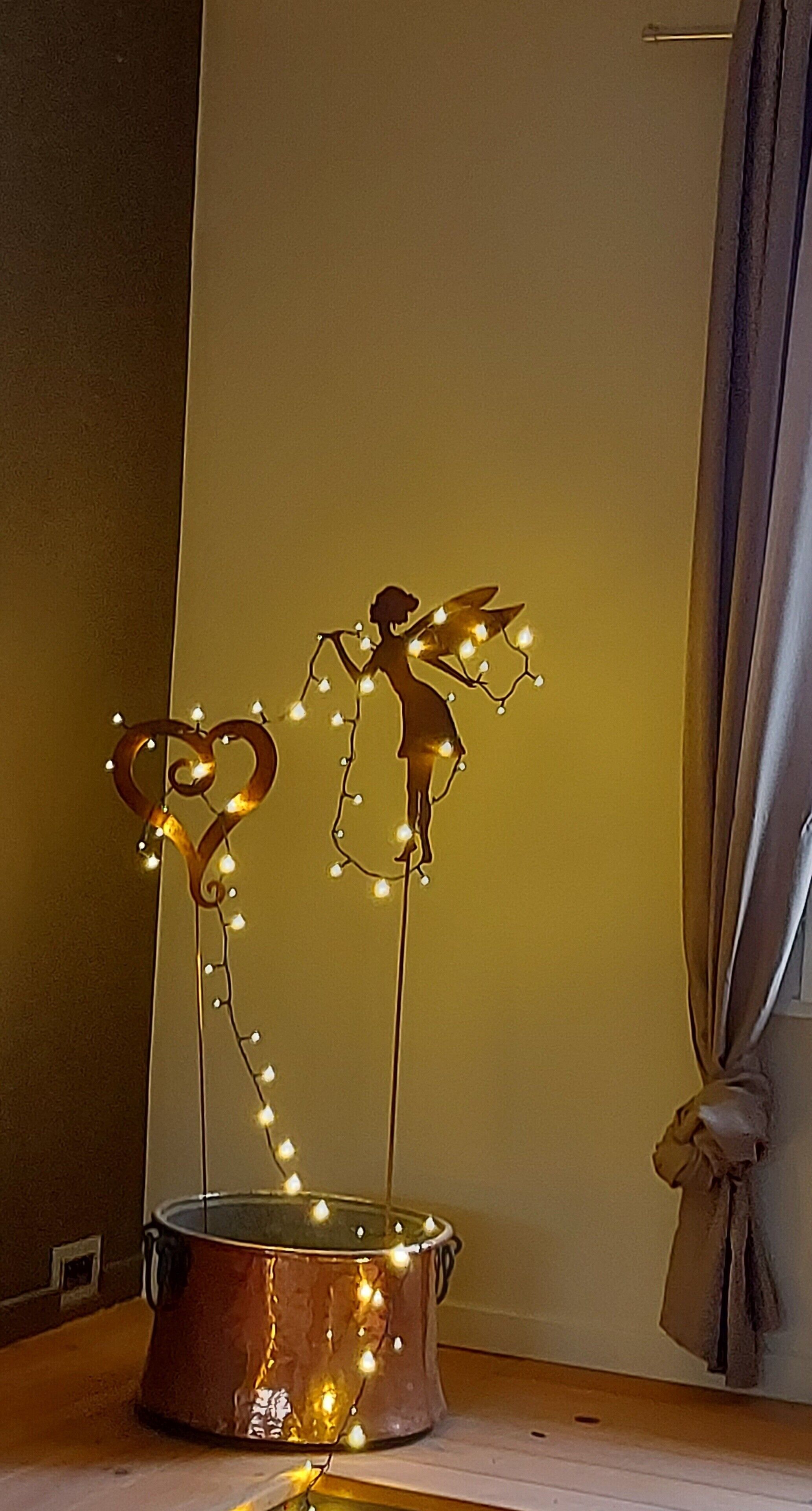 A decorative item with a silhouette of a person and heart-shaped figures, placed on a surface with a curtain in the background.