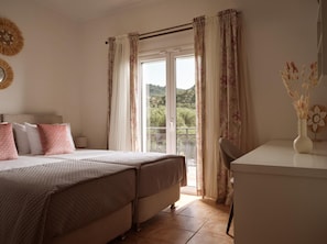 A bedroom with two beds, a desk, and a view of a balcony with a railing. - Ilision – Contemporary Living Apartment (Zakynthos)
