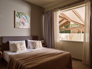 Un dormitorio con cama, almohadas, mesita de noche, un cuadro y una ventana con cortinas.