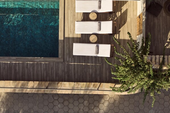 An aerial view of a rooftop pool area with three lounge chairs and a wooden deck.
